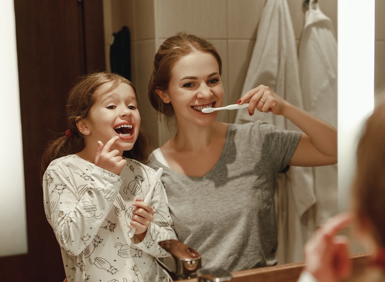 Woman smiling with daughter brushing teeth